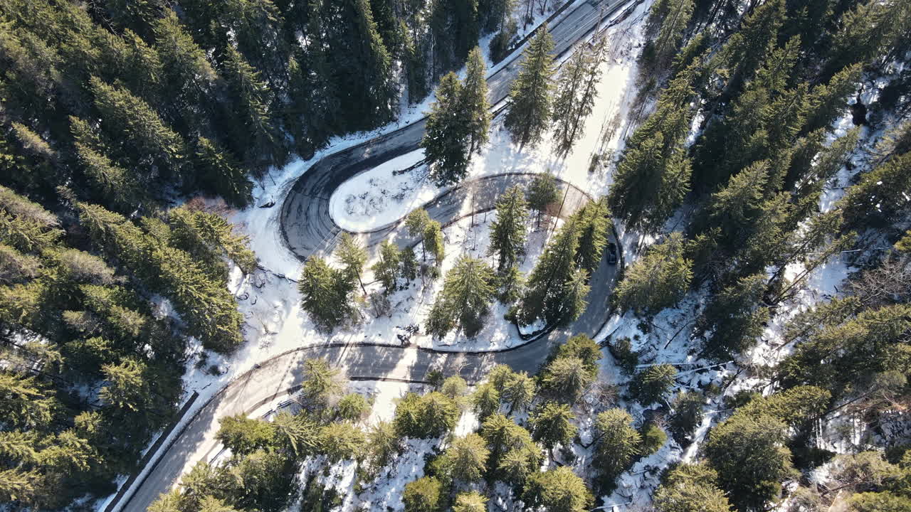 Aerial drone view of the spring Carpathians, Romania. Valley with road and moving cars, forest partly covered with snow