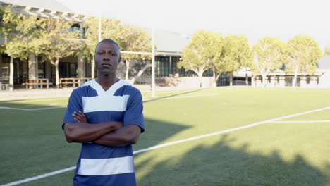 standing on football field, african american male athlete in crossing arms confidently, copy space