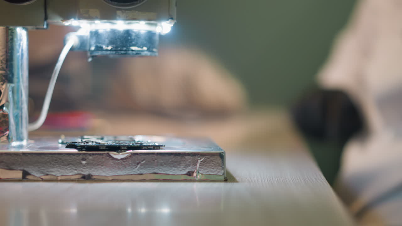 A close-up view of a microscope focusing on a circuit board with LED lights illuminating the workspace, the background is blurred