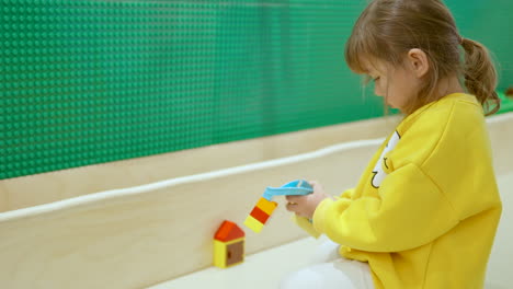 preschool girl playing with blocks focuses on attaching piece to her creation