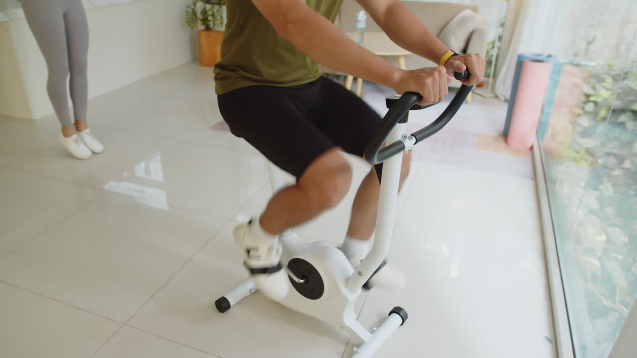 Man Exercising on Fitness Bike while Woman Jumping Rope at Home