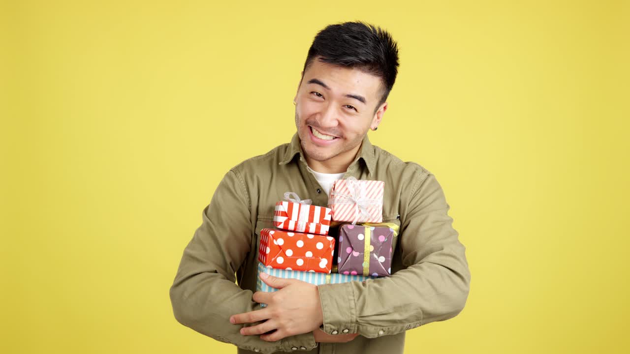 Happy Asian Man Holding a Stack of Gifts on Yellow Background