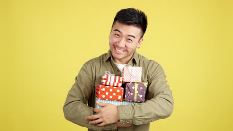 happy asian man holding a stack of gifts on yellow background