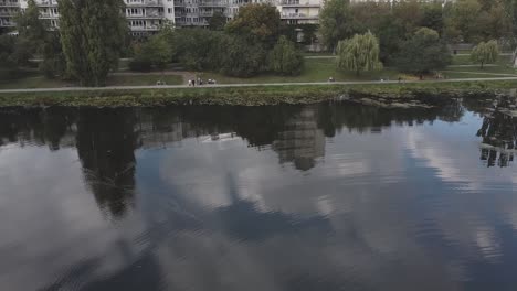 Drone-video-of-lake-and-forest-with-building-and-trees,-cloud-reflections-on-lake