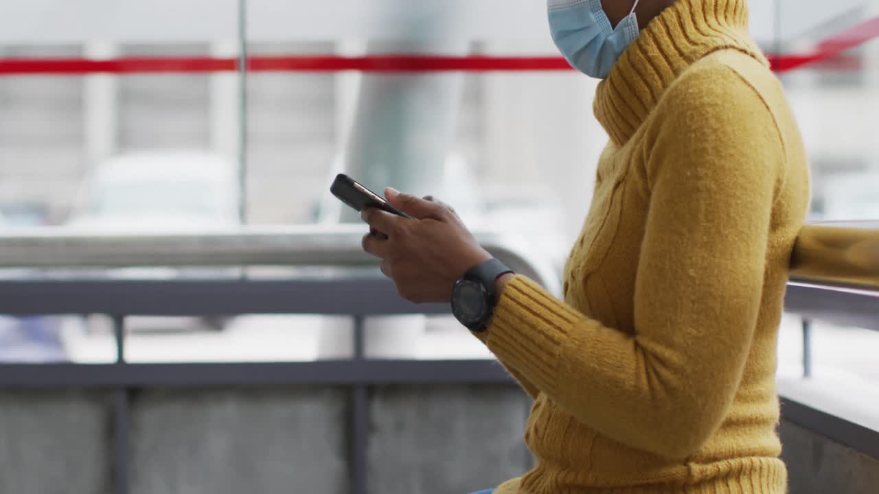 mujer de negocios afroamericana con máscara facial usando un teléfono inteligente