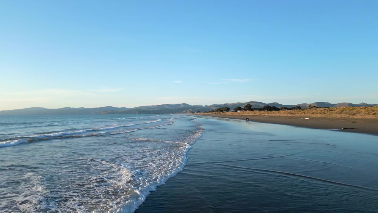紐西蘭基督城布萊頓海灘與遠處港口山丘沐浴在晨光中，4K 60FPS 無人機跟拍