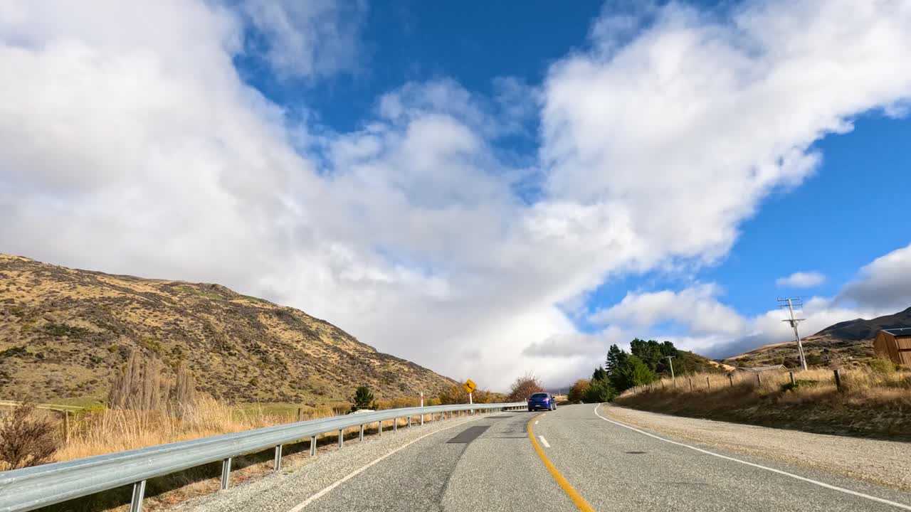 A picturesque drive through Wanaka, New Zealand, showcasing vibrant autumn foliage and mountainous terrain under a bright blue sky