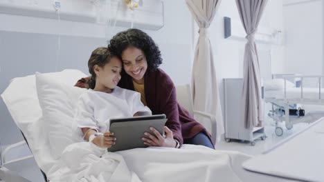 Happy-biracial-mother-with-her-sick-daughter-patient-using-tablet-in-hospital-in-slow-motion