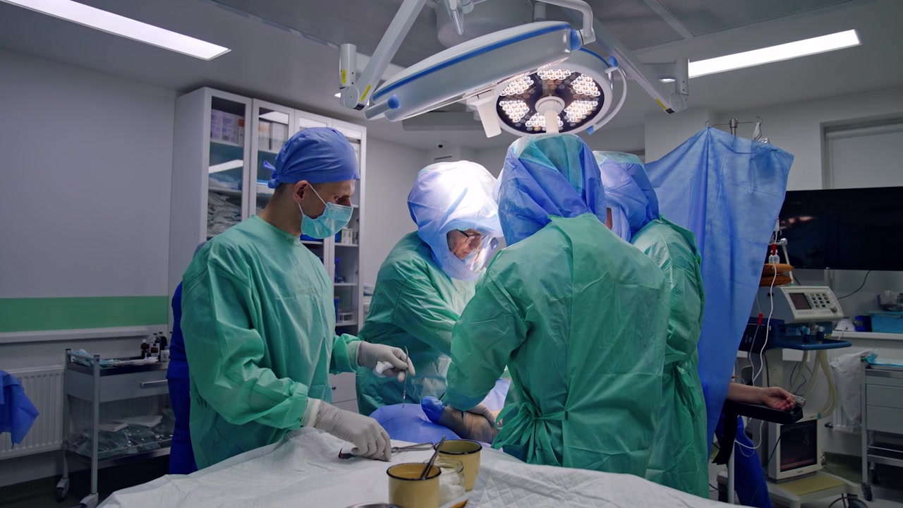 Arthroscopic operation on a leg in modern clinics. Assistant passes the metal tools to the team of surgeons wearing protective helmets.