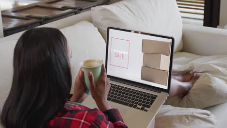 Biracial-woman-on-couch-with-coffee,-using-laptop-for-online-shopping,-slow-motion