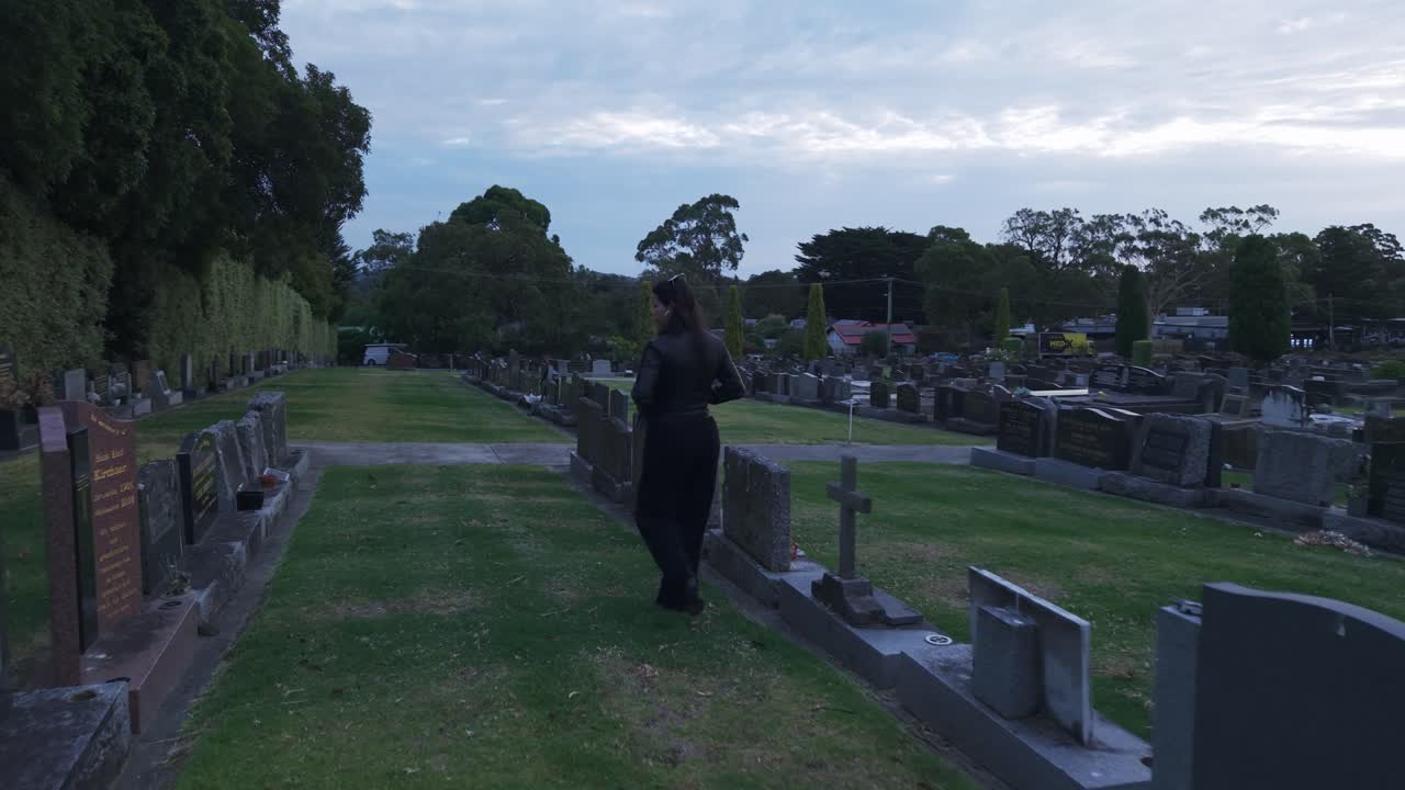 Una donna cammina attraverso un cimitero sereno a Ferntree Gully, Melbourne, sotto un sole al tramonto. L'atmosfera pacifica è colta in una ripresa a seguire dinamica con illuminazione naturale.