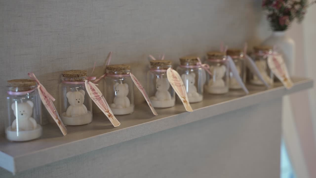 핑크색 리본으로 장식 된 선반에 테디 베어 불이 있는 작은 유리 항아리 줄
