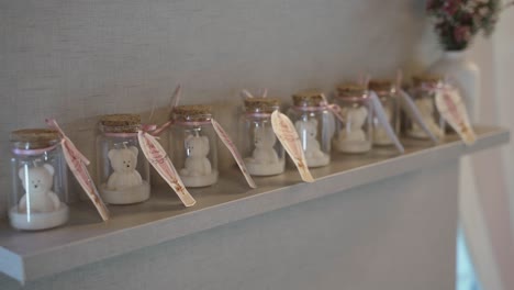 row of small glass jars with teddy bear candles on a shelf, decorated with pink ribbons