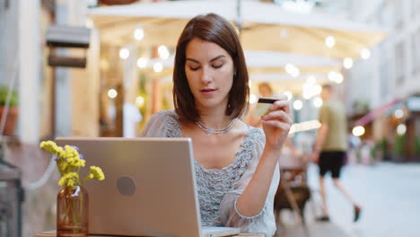 Young-woman-using-credit-bank-card-laptop-computer-while-transferring-money-order-food-in-cafeteria