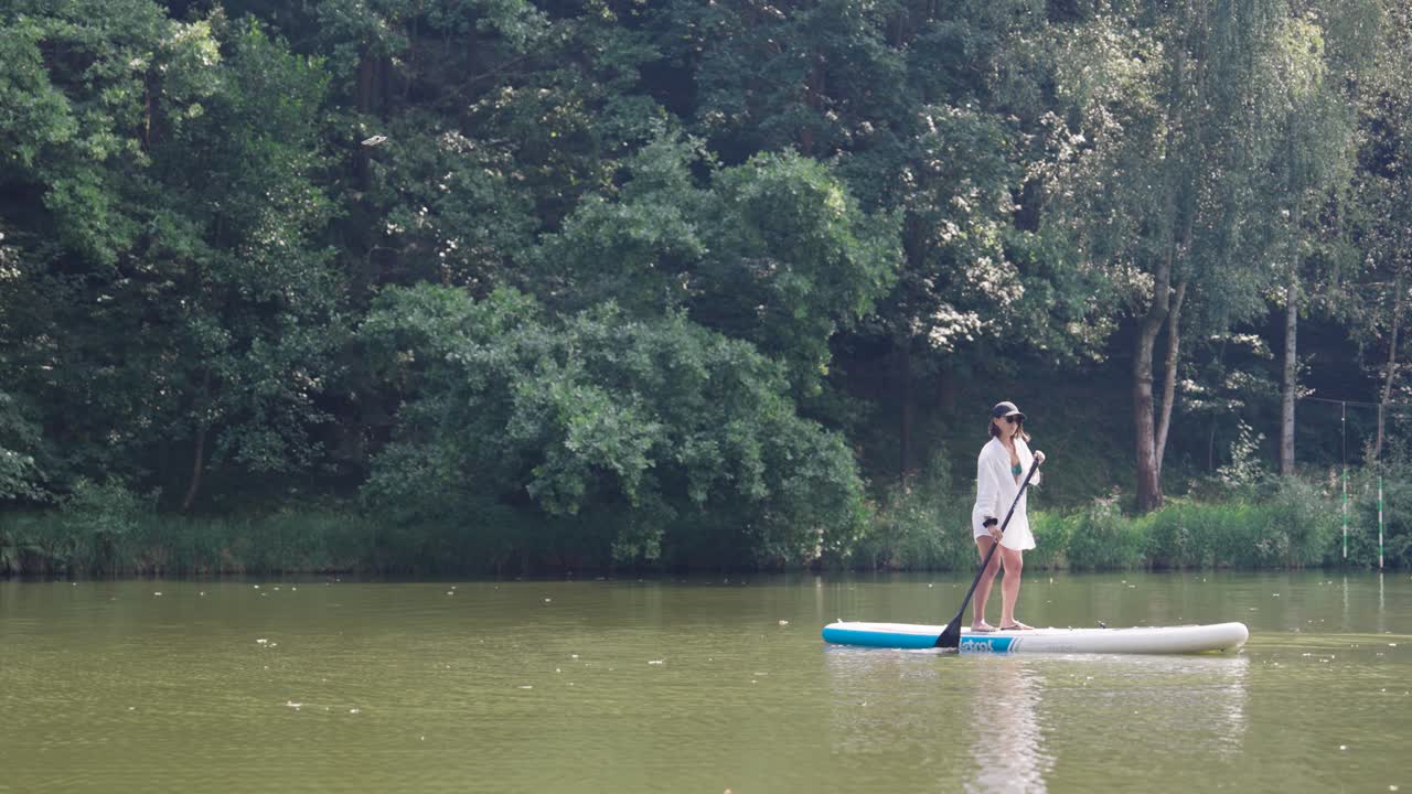 Female use stand up paddle board in river with forest background, Czechia