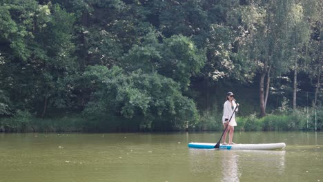 female use stand up paddle board in river with forest background, czechia