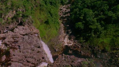 stunning aerial view of a waterfall cascading down rocky cliffs in a lush green forest in chapada dos veadeiros, brazil, creating a rainbow in the mist, slow moton drone shot