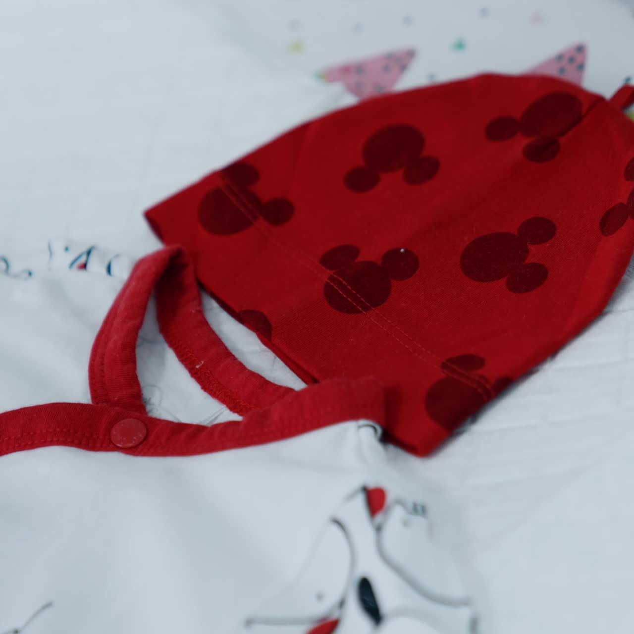 Red cap and white bodysuit with letters on the table. Pieces of clothes for a newborn child. Close up