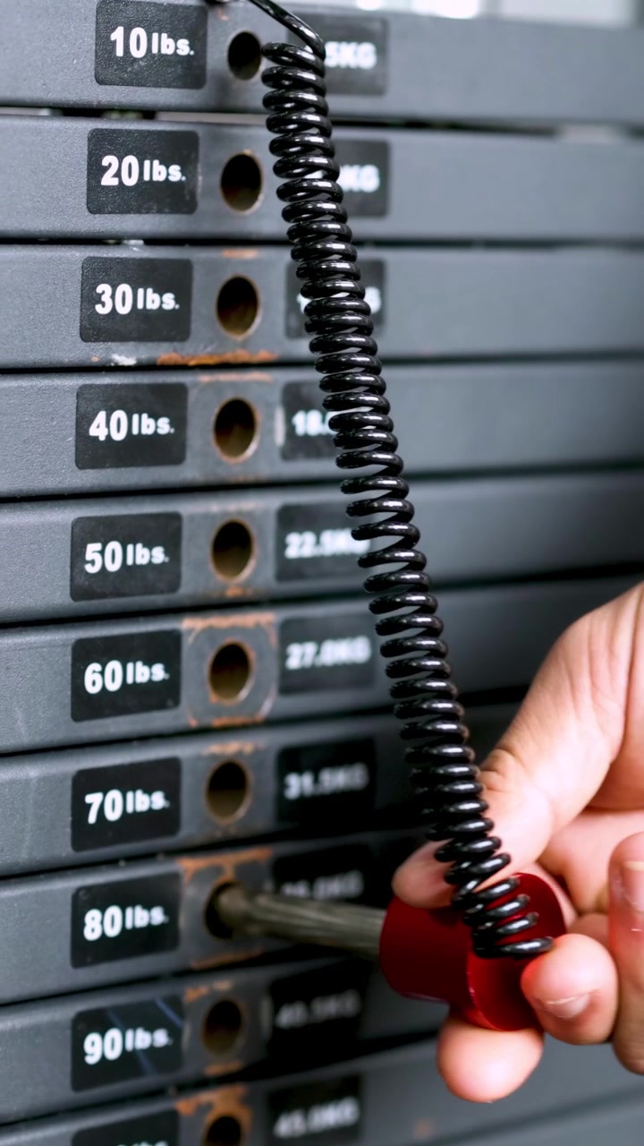 A hand adjusts the pin on a weight stack, selecting different weights for exercise equipment in a gym setting
