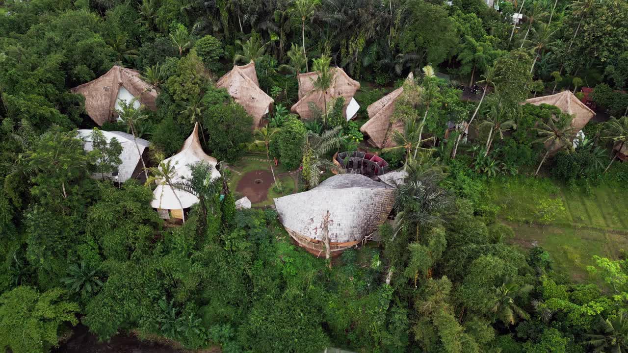 Vista aerea con drone di un villaggio nella foresta tropicale con architettura organica e case con tetto di paglia, immerso in una fitta vegetazione della giungla, che crea un rifugio appartato nella foresta pluviale a Bali, Indonesia