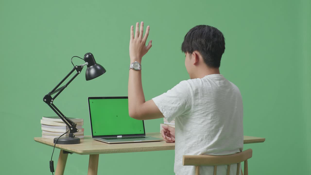 젊은 남성이 손을 들고 집에서 녹색 스크린 배경에서 녹색 화면 노트북에 타이핑하는 동안 말하고 있습니다.