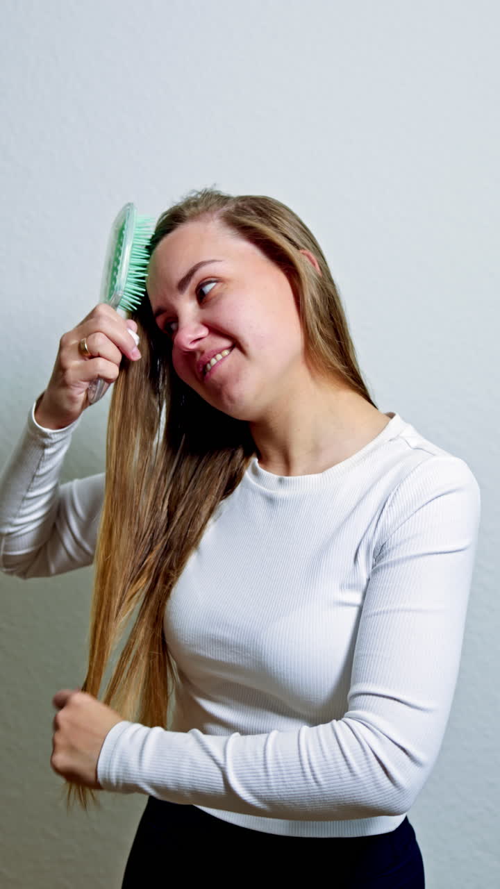 Beautiful healthy hair after cosmetic procedures. Smiling beautiful woman combing long shiny hair with comb in the morning. Hair care