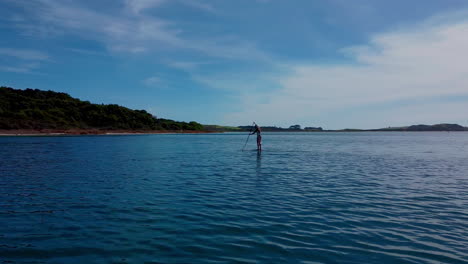 Drone-shot-moving-around-a-paddle-boarder-on-a-lake-at-Kai-Iwi-lakes,-New-Zealand