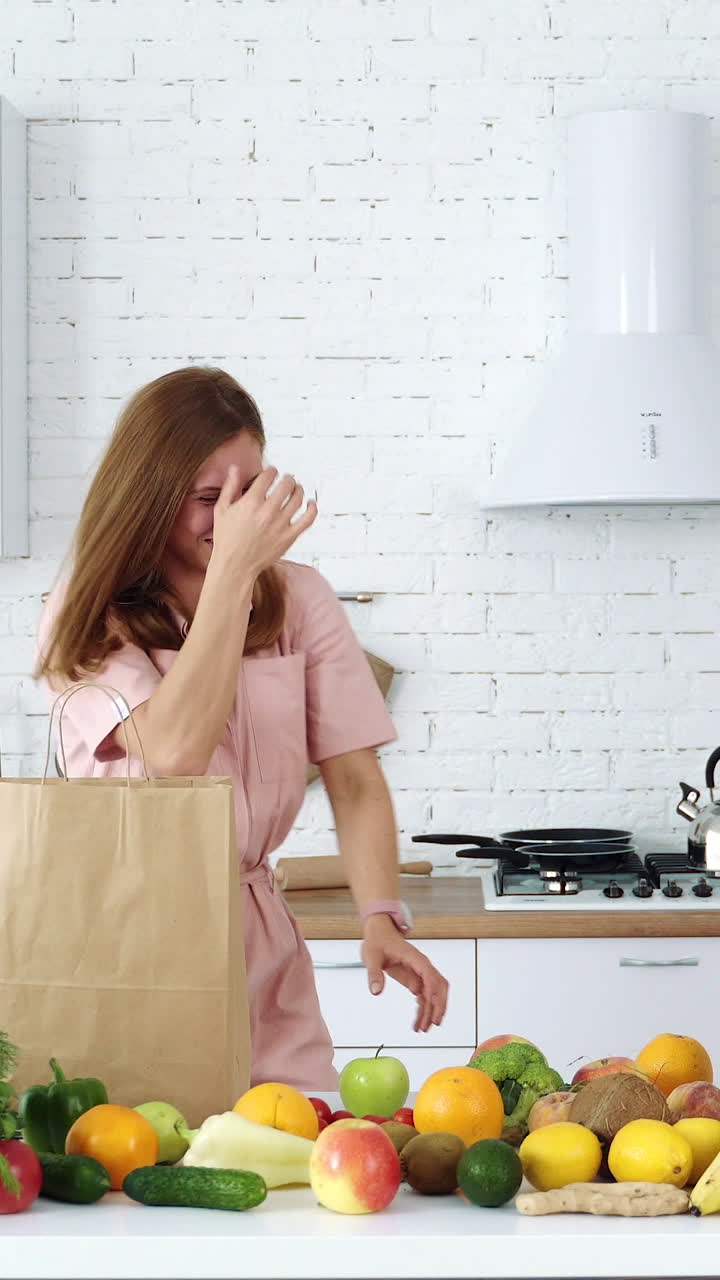 Joyful girl in the kitchen plays and throws apples. Unsuccessful game. Healthy eating concept. Woman on a diet. Vertical video