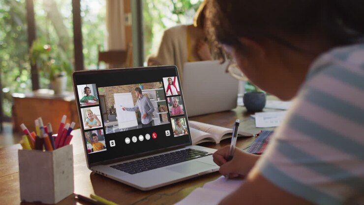 Schoolgirl using laptop for online lesson at home, with diverse teacher and class on screen
