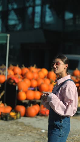 woman in a pink shirt and denim overalls, surrounded by pumpkins