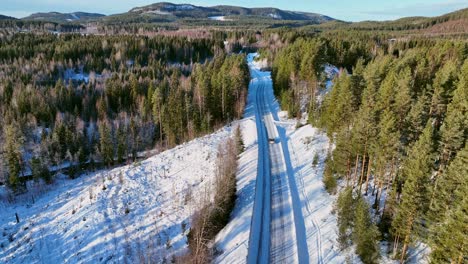 Coche-En-Una-Carretera-Nevada-En-Medio-De-Un-Bosque-De-Pinos-En-Skorped,-Suecia,-Con-Sombras-Que-Se-Extienden-Por-El-Paisaje,-Vista-Aérea