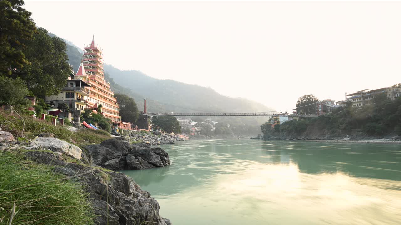Stunning time lapse video of the Ganga river embankment with the Lakshman Jhula bridge and the Tera Manzil Temple (Trimbakeshwar) during a beautiful sunset. Rishikesh, Uttarakhand, India.