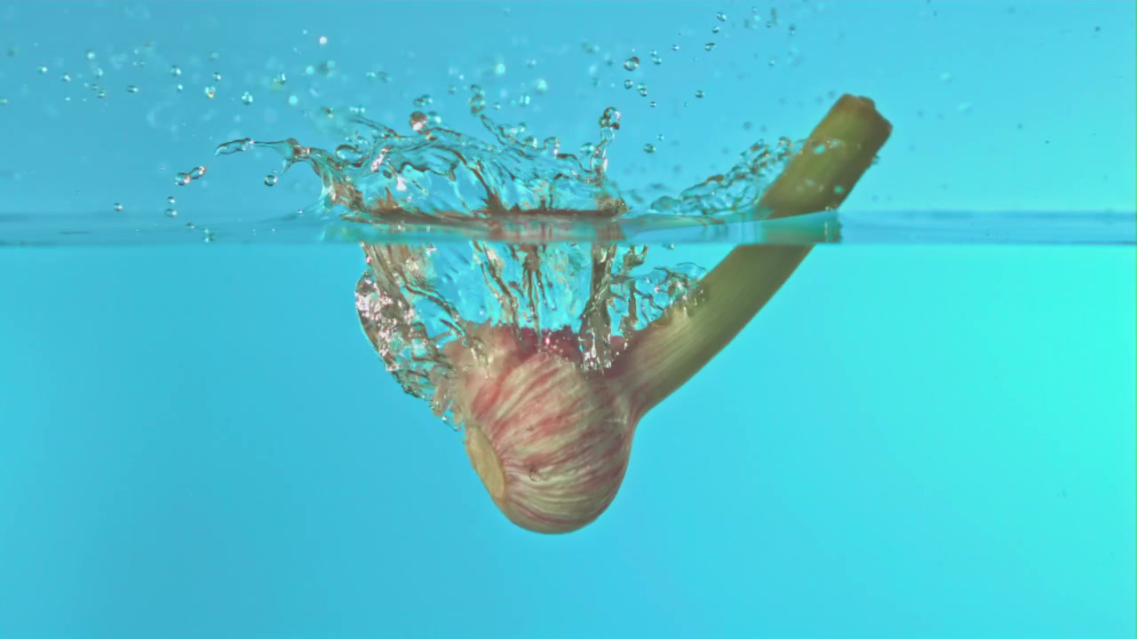 Frisk hvidløg falder ned i vand med plask i slowmotion