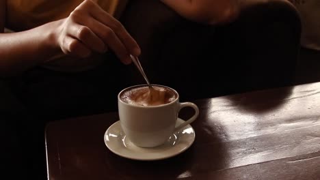 Mujer-Removiendo-Tranquilamente-Una-Taza-De-Capuchino-Mientras-Se-Relaja-En-Un-Acogedor-Café,-Ambiente-Otoñal-Y-Estética