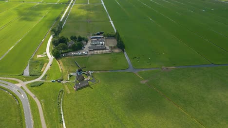 scenic drone footage showing a traditional dutch windmill located at a rural intersection, surrounded by expansive green farmland and cycling paths
