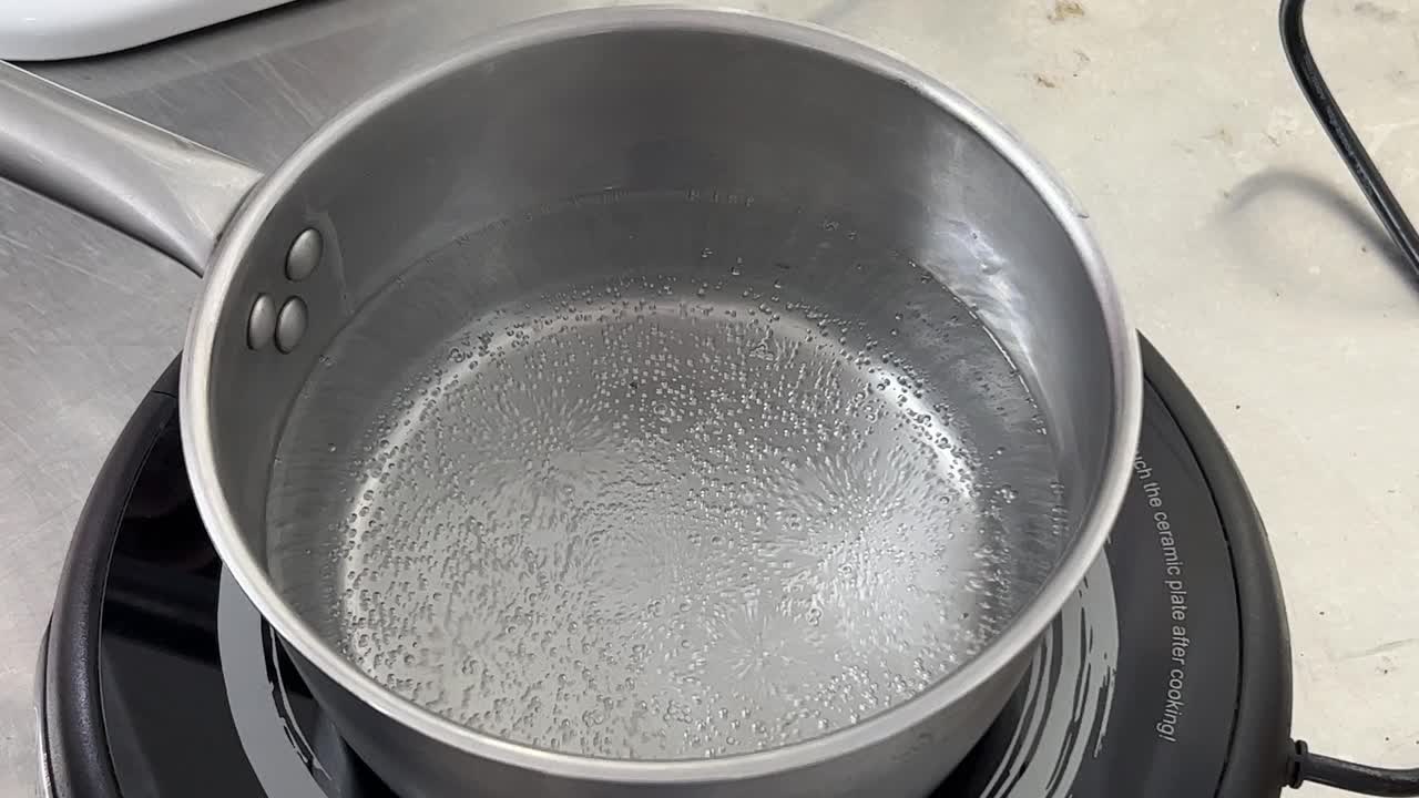 Pot of water boiling and bubbling on electric cooktop, preparing to make Swiss meringue buttercream