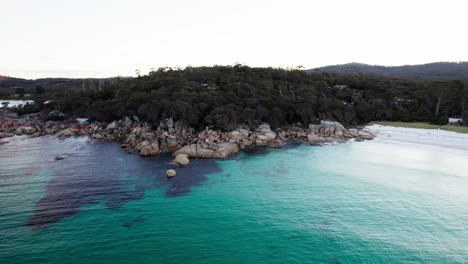 Aerial-turquoise-blue-ocean-with-fiery-red-rock-coastline-and-forest