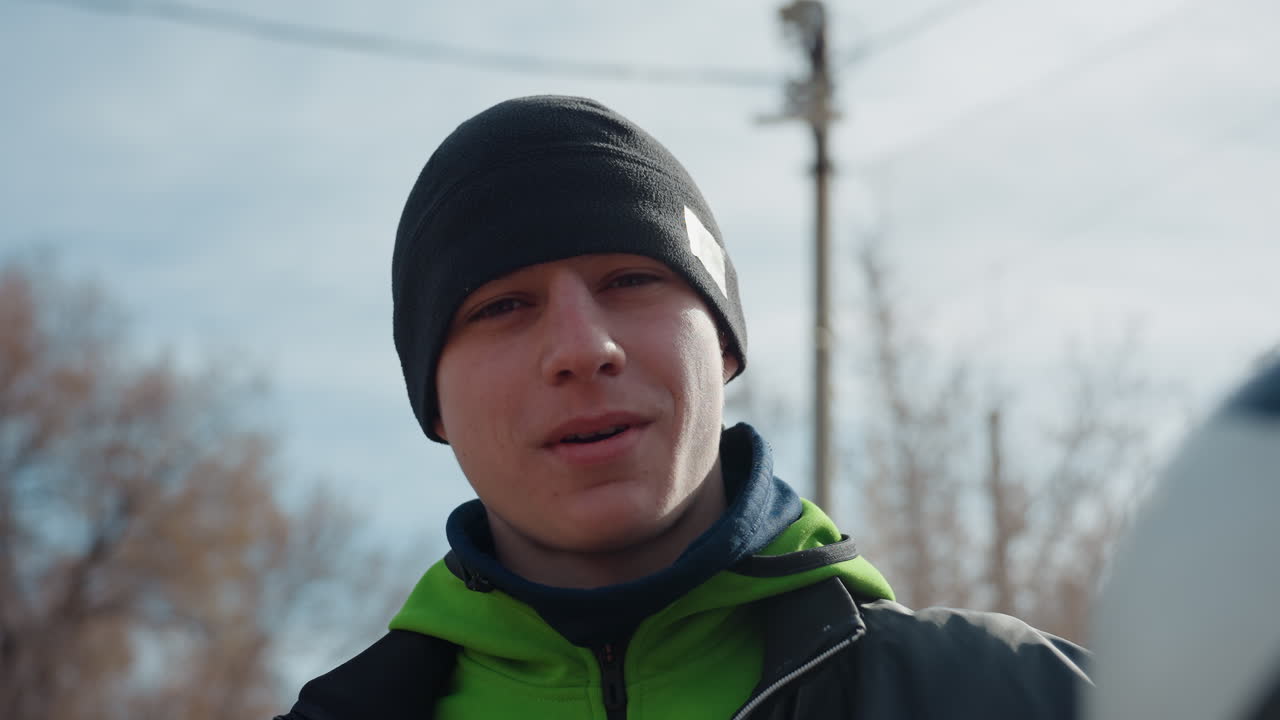 축구공 장면, 울타리 옆 어린 운동선수에게 얕은 심도로 초점을 맞추고, 공과 패션 디테일을 강조한 역동적인 도시 풍경, 도시 배경과 의상을 갖춘 청소년 스포츠 순간을 생생하게 묘사