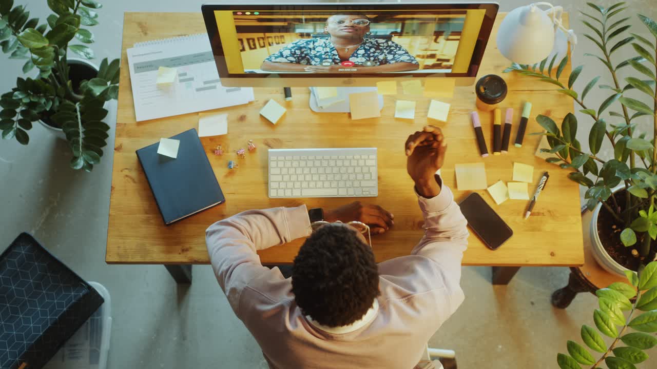 Top Down of Man Video Calling with Colleague on Computer at Office Desk