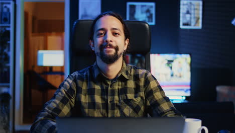 Smiling-man-sitting-on-chair-at-home-office-desk-in-neon-illuminated-apartment