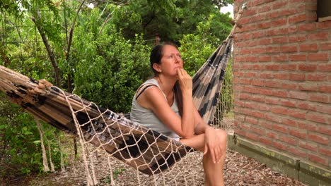 mujer caucásica sentada y relajada en una hamaca fuera de la casa