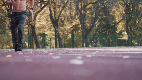 healthy athlete is running in the stadium. young sportsman is involved in sport running on the autumn trees background. view from below.