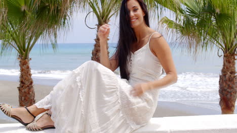 Woman-in-White-Dress-Sitting-on-Beach-Wall