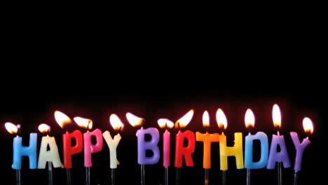 colourful happy birthday candles being blown out on black background