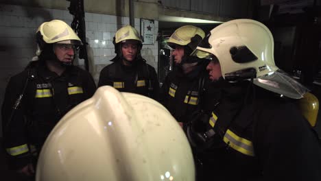 group of five firefighters wearing full equipment in smokey area. relaxed chatting after work well done. fire trucks in the background. name tag translation is fireman and model's last name.