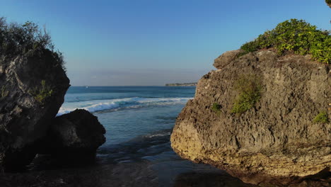 Flying-between-two-large-rock-formations-at-the-coast-–-surrounded-with-nature-on-a-sunny-day