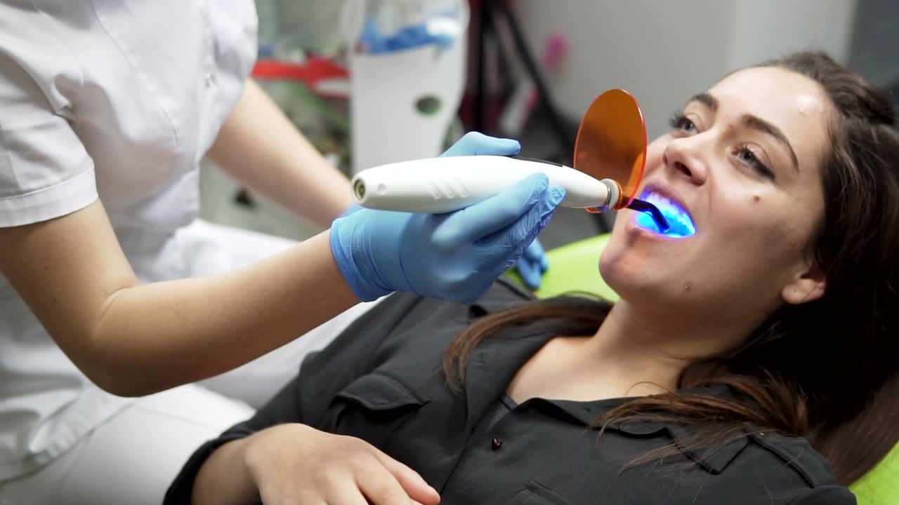Young female patient with open mouth receiving dental filling drying procedure