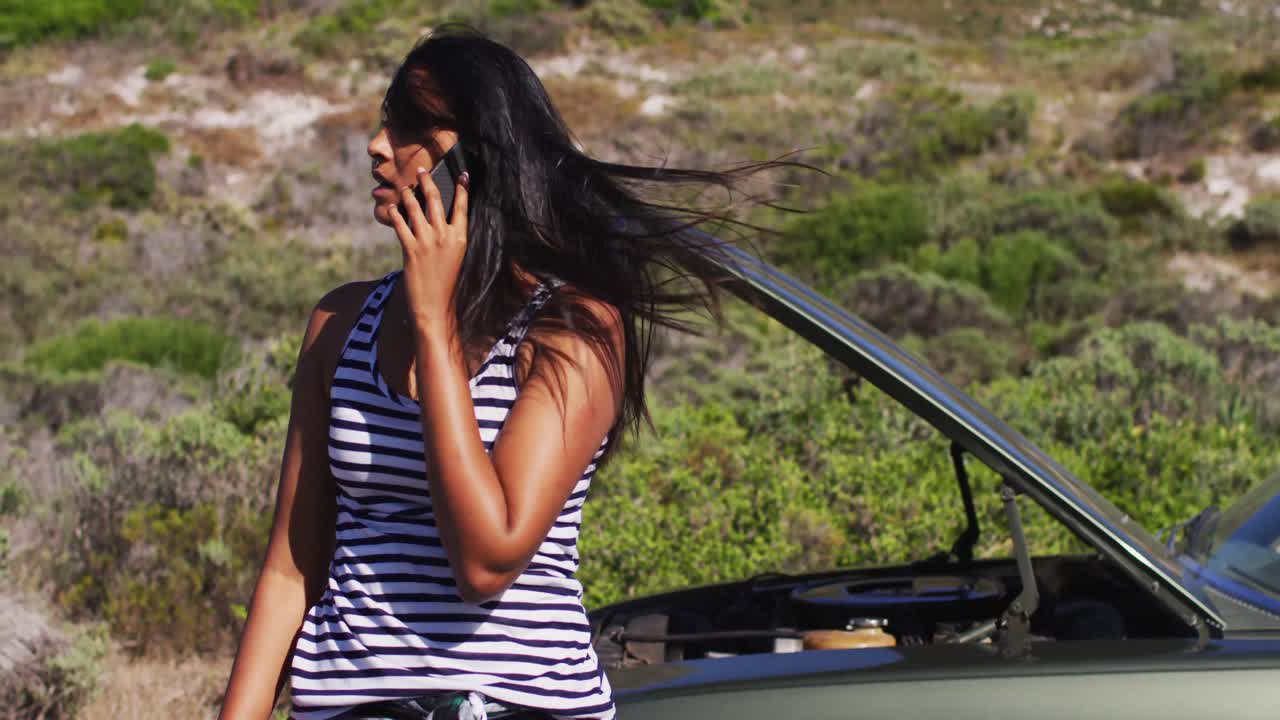 아프리카계 미국인 여성 이 도로 에 있는 망가진 차 근처 에 서서 스마트폰 으로 이야기 하고 있다