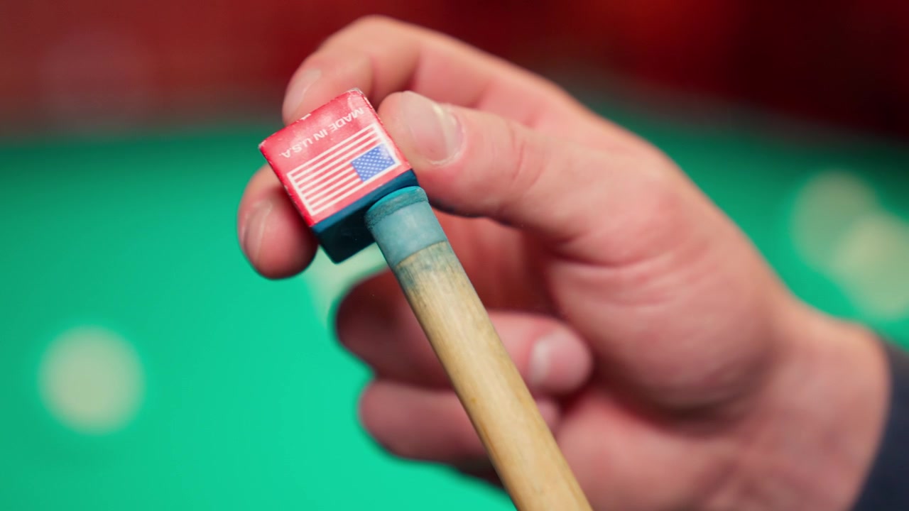 Nærbillede af hånd, der kridter en billardkø med kridt med amerikansk flag