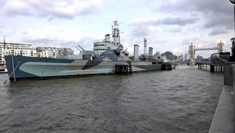 hms belfast, slow motion of a royal navy light cruiser docked on river thames on a background of tower bridge under cloudy sky in london, uk